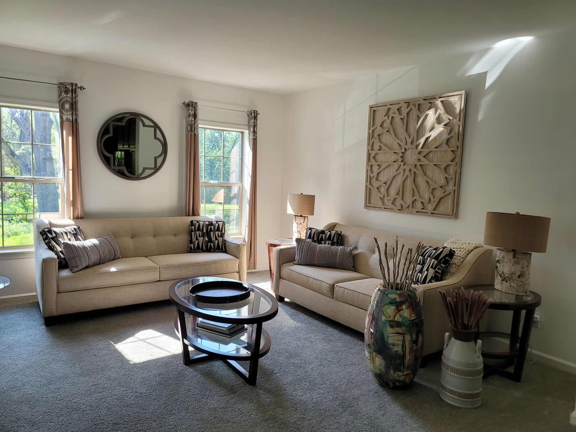 Living room with two beige couches, round coffee table, and decorative wall art.