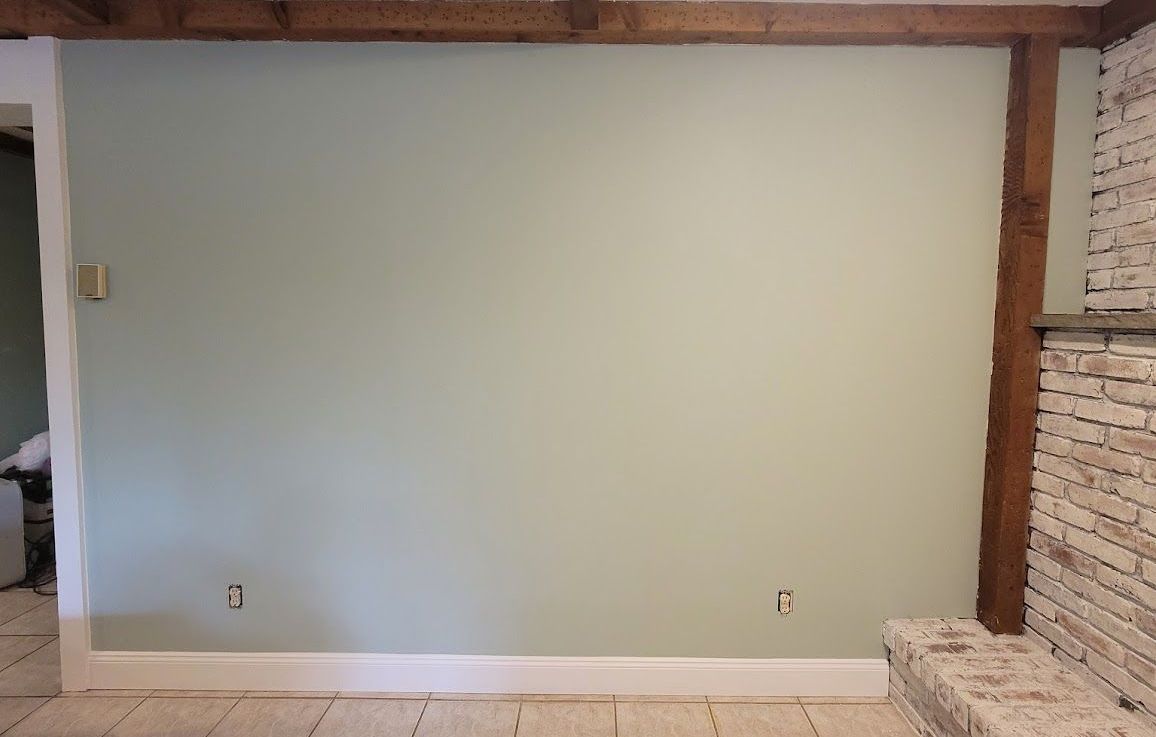 Light green wall with wooden beam, white trim, and a brick fireplace.