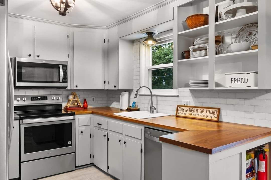 White kitchen with stainless steel appliances, wooden countertops, and open shelving.
