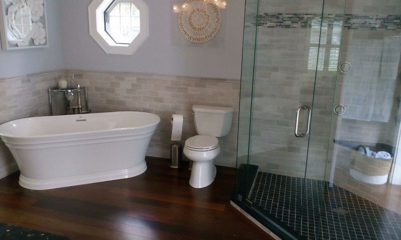 Bathroom with white freestanding tub, toilet, glass shower, and wood floor.