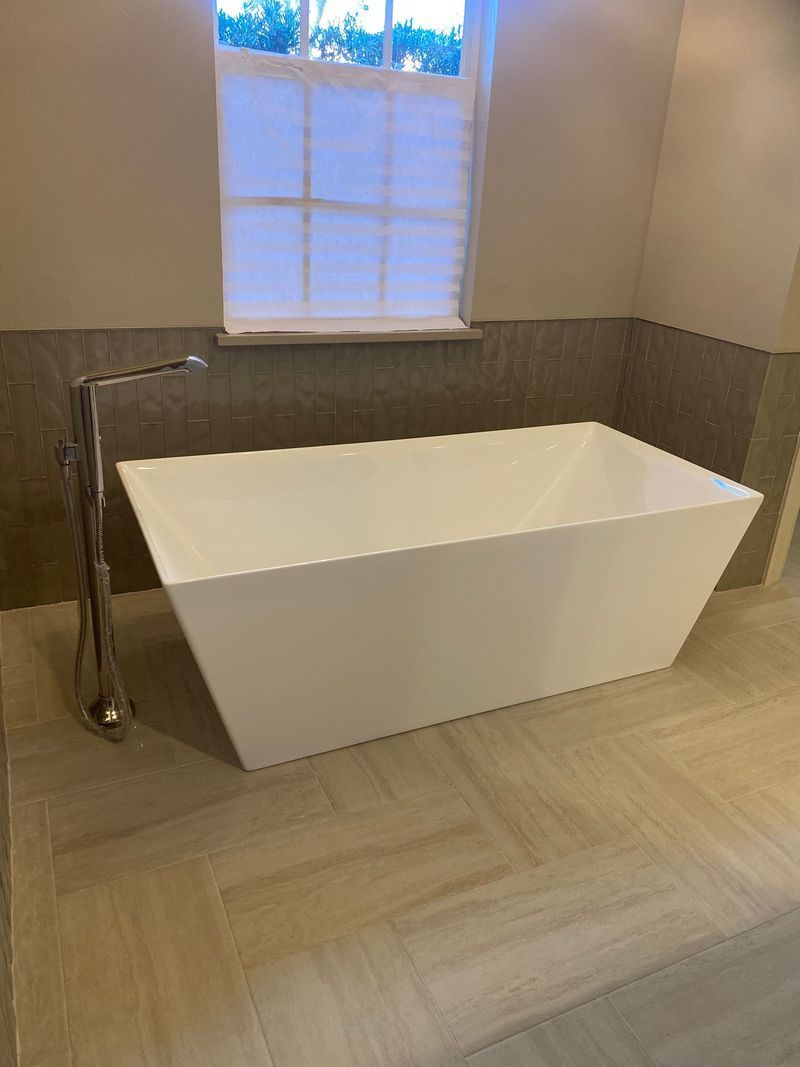 White rectangular soaking tub near a window, tiled floor, chrome faucet.