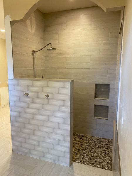 Open shower with light-colored tile walls, pebble floor, and glass-tiled partition.