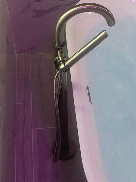 A freestanding chrome bathtub faucet with a handheld shower next to a white bathtub filled with water.
