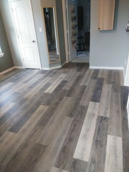 Room with diagonally laid wood-look flooring. White door, gray walls, and hallway visible.