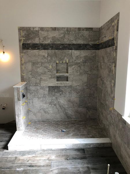 Newly tiled shower with gray tiles and dark accent stripe; unfinished construction.
