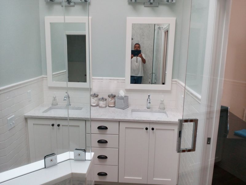 Bathroom with white vanity, mirrors, and glass shower enclosure. Person reflected in mirror.