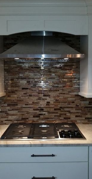 Kitchen with stainless steel hood, mosaic tile backsplash, and gas stovetop. White cabinets and light countertop.