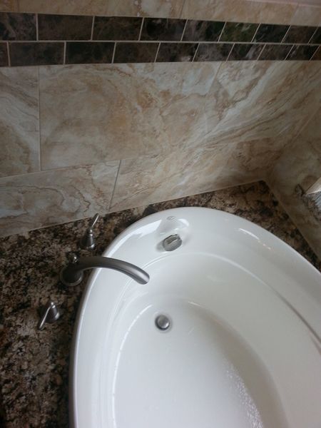 White bathtub with silver faucet, set in a bathroom with marbled tile and brown countertop.