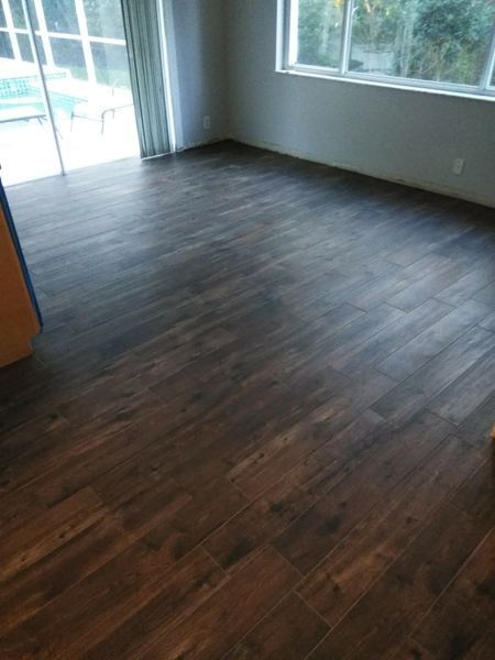 Dark wood-look flooring in a room with a sliding glass door and windows, leading to an outdoor pool area.