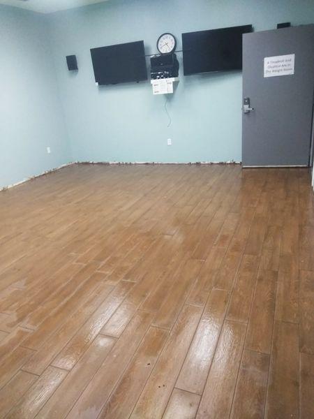 Empty room with wood-look flooring, light blue walls, two mounted TVs, a door, and a clock.