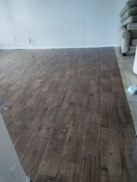 Dark brown wood-look tile flooring in a room with white walls and a glimpse of a beige couch.