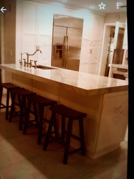 Kitchen island with stools; stainless steel fridge, light cabinets, marble countertop, dark stools.