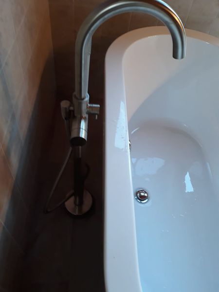 Bathtub with silver faucet and drain, next to a tile wall.
