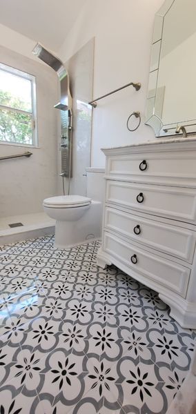 Bathroom with white vanity, floral patterned floor tiles, toilet, and shower.