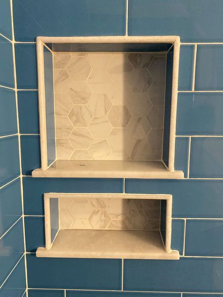 Two rectangular recessed shower niches. Blue tiled wall with marble trim.