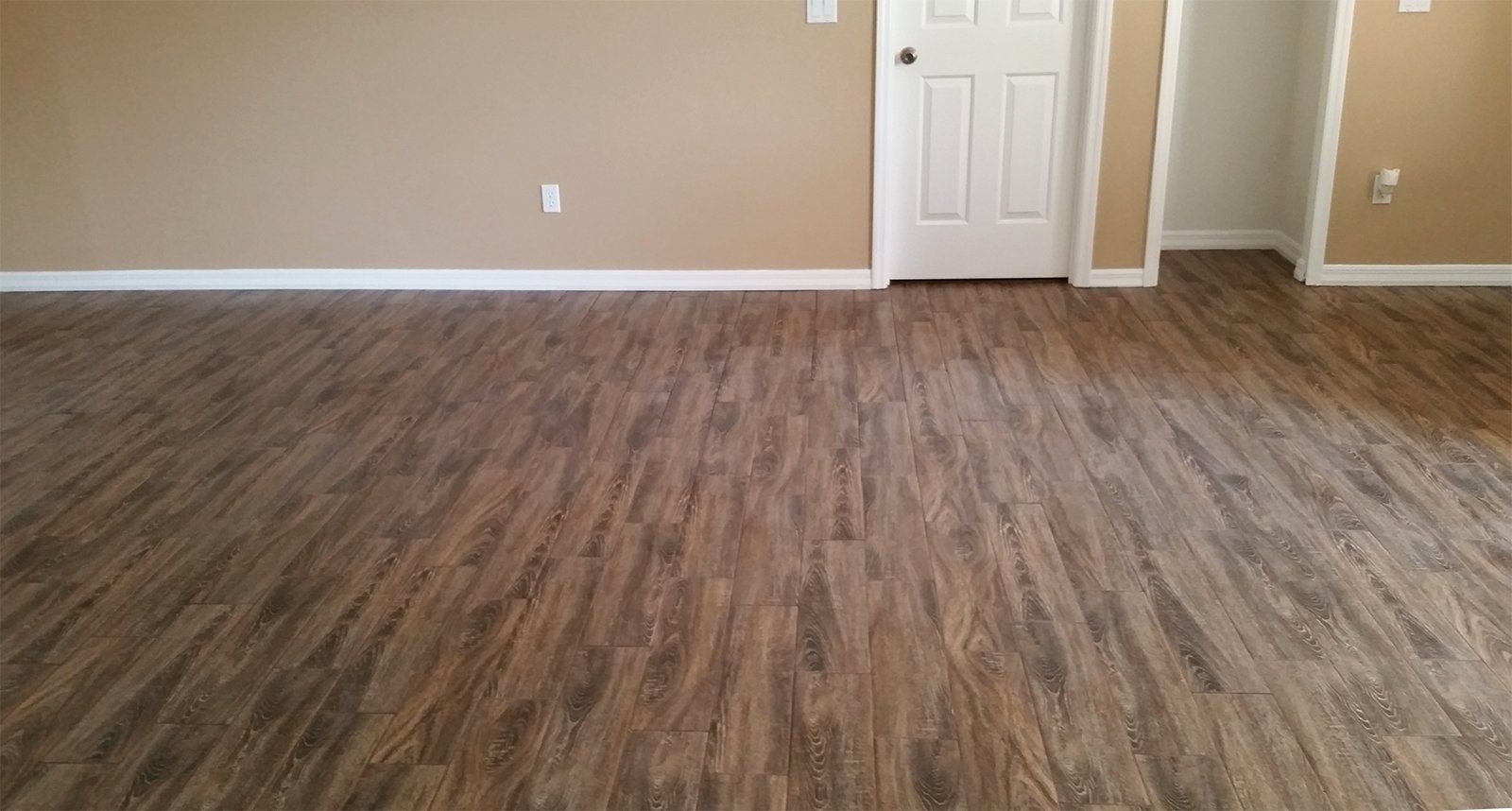 Room with wood-look flooring, beige walls, white trim, and a white door.