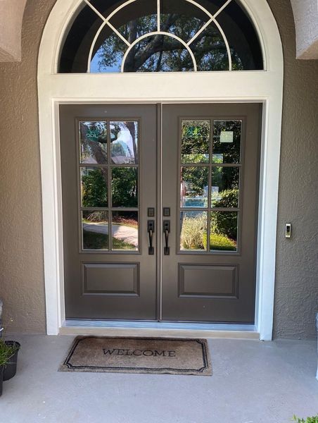 Double brown front doors with glass panes and arched transom window, white trim.