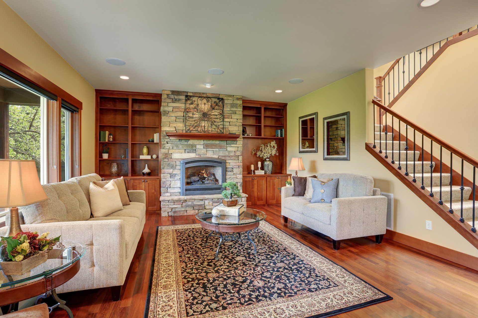Living room with fireplace, built-in shelves, staircase, and two couches on hardwood floor.