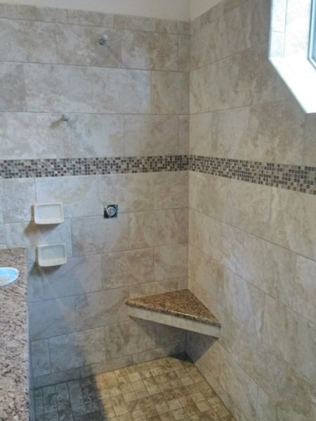 Tiled shower with corner seat and decorative band. Light brown tiles, beige granite, and a window.