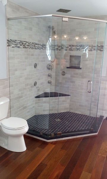 Modern bathroom with glass shower, toilet, and wooden floor. Shower has tiled walls, black tile floor, and multiple showerheads.