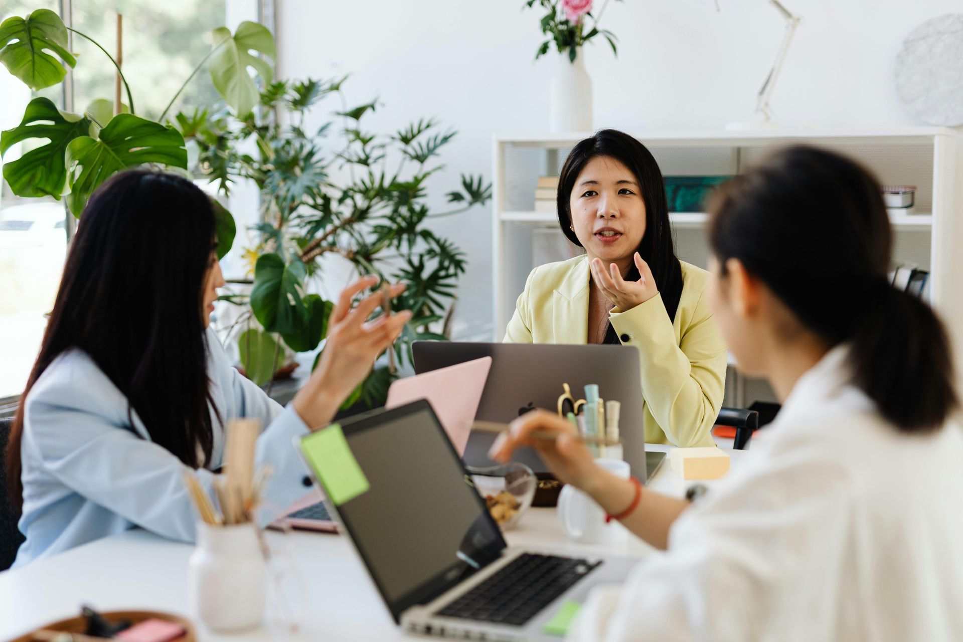 Four people sit at a wooden table in an office, reviewing documents and working on a laptop during a collaborative meeting.