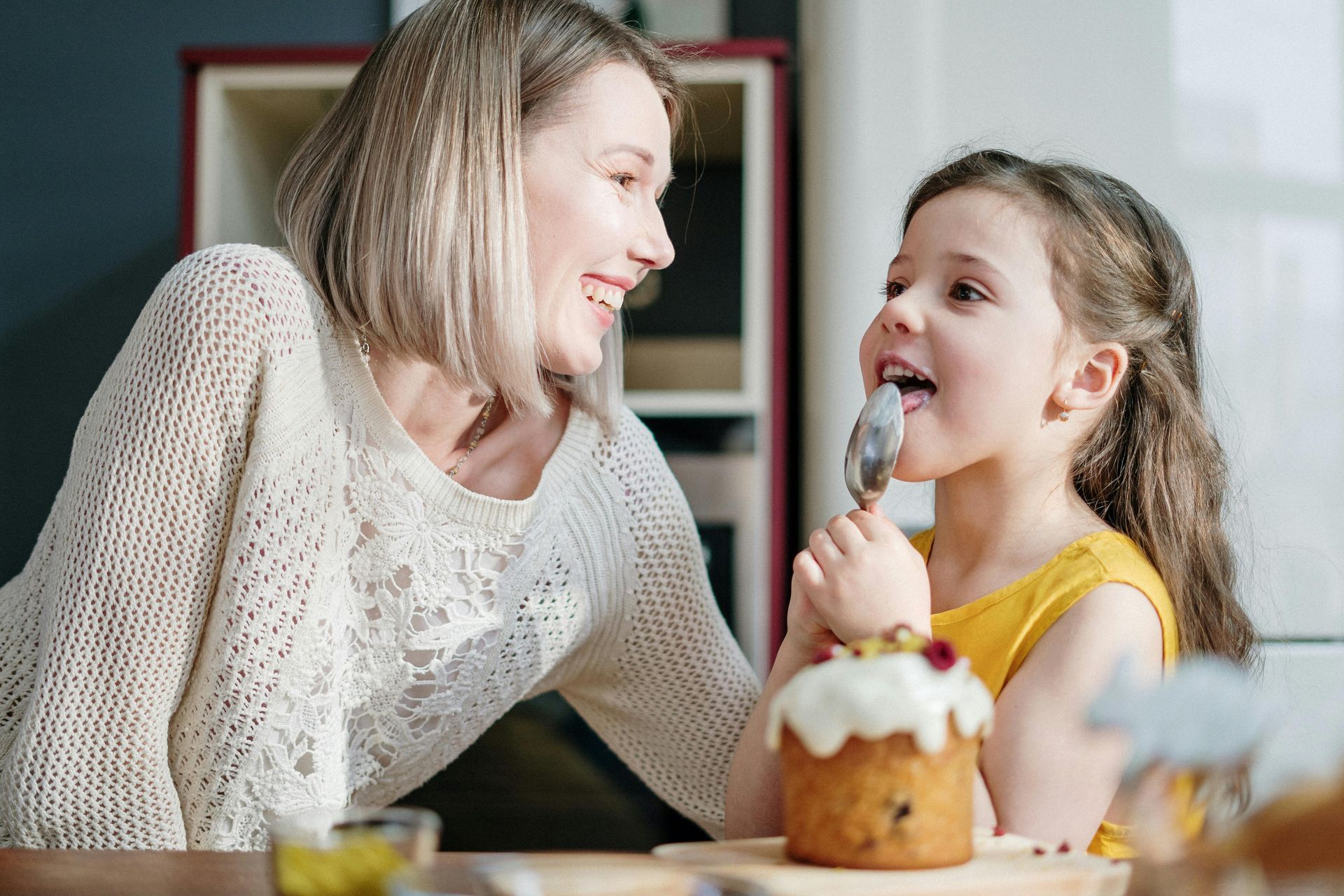 A woman and a little girl are eating a cake together.