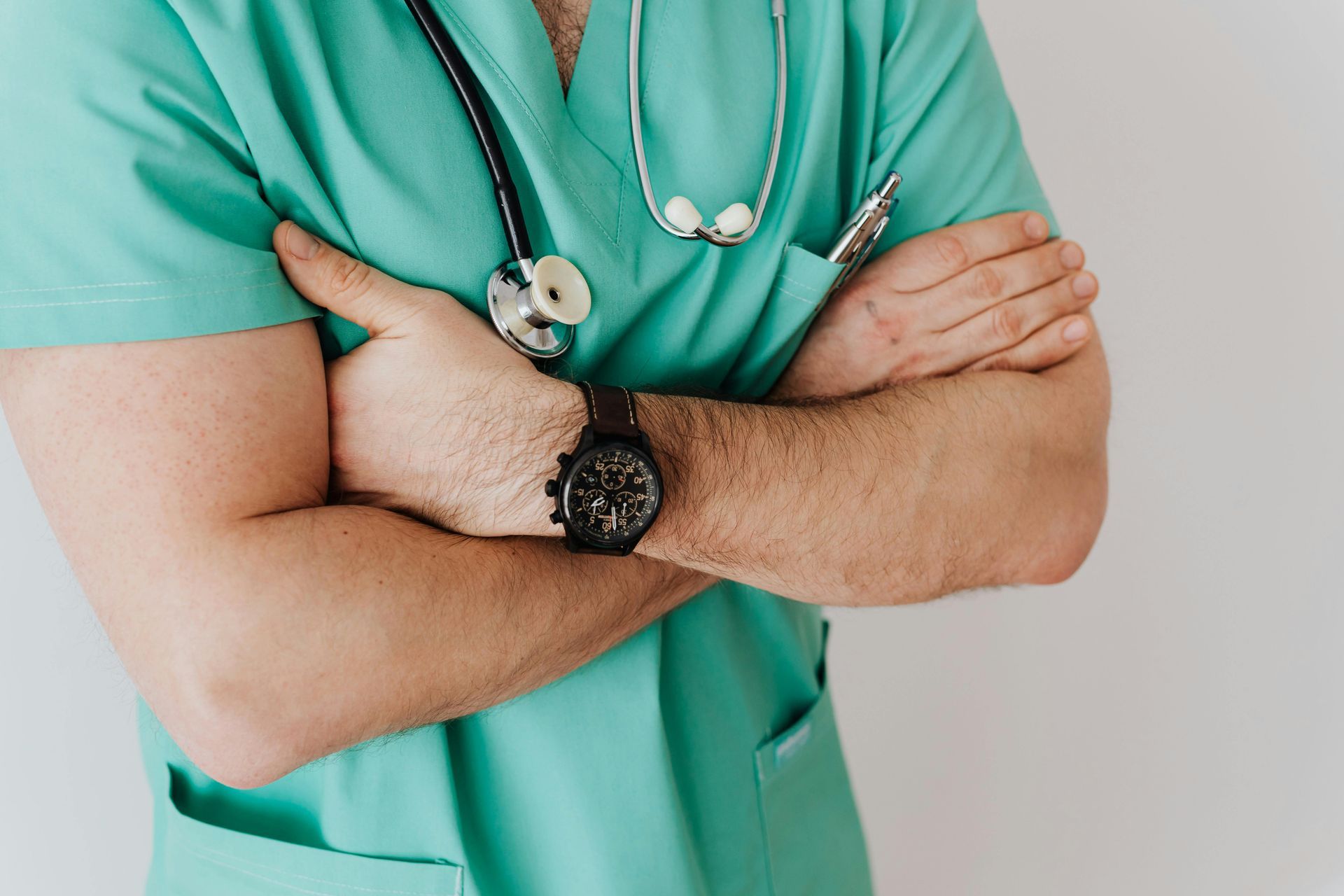 A man in a green scrub with a stethoscope around his neck is standing with his arms crossed.