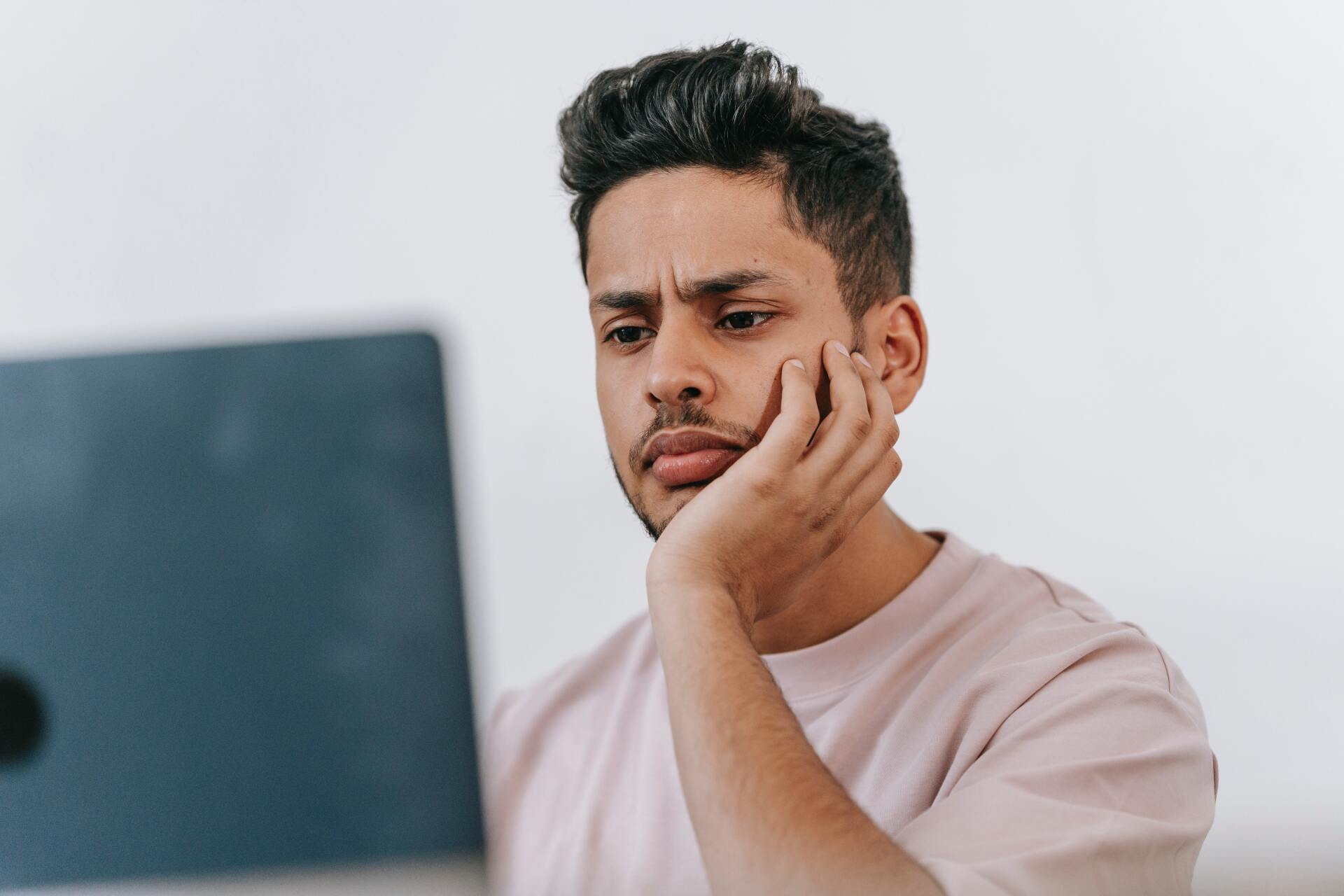 a man is sitting in front of a laptop computer with his hand on his face .
