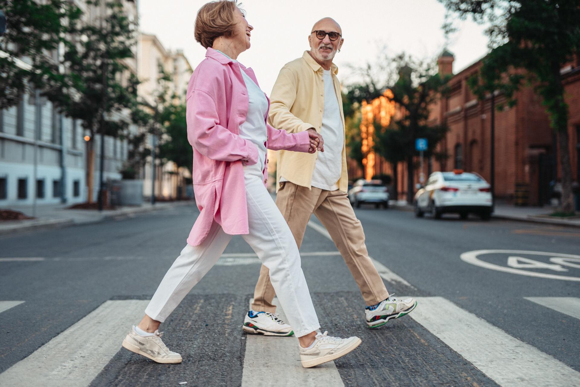 an elderly couple is crossing the street while holding hands .