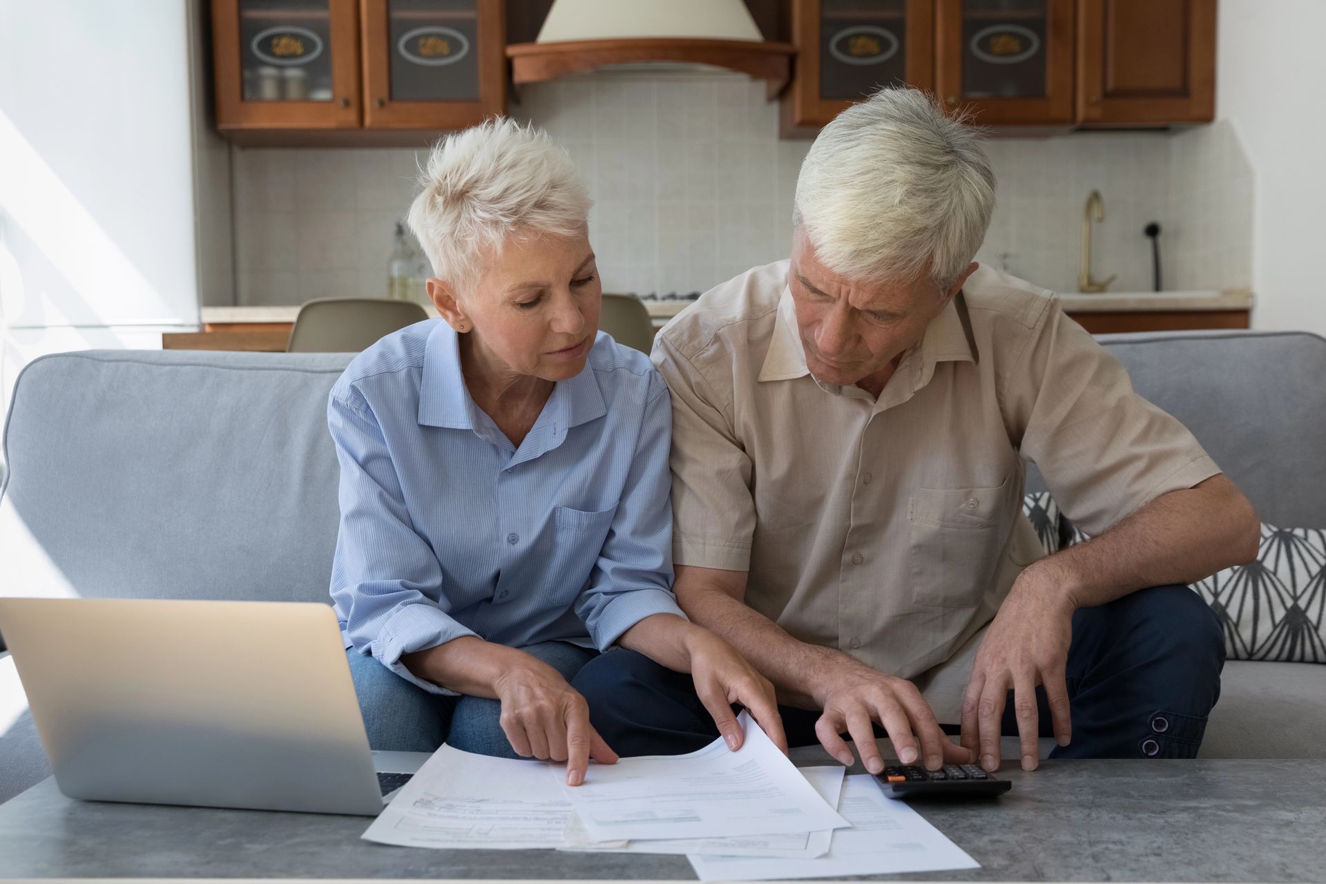 Two people reviewing papers and typing on a laptop on a couch in a living room
