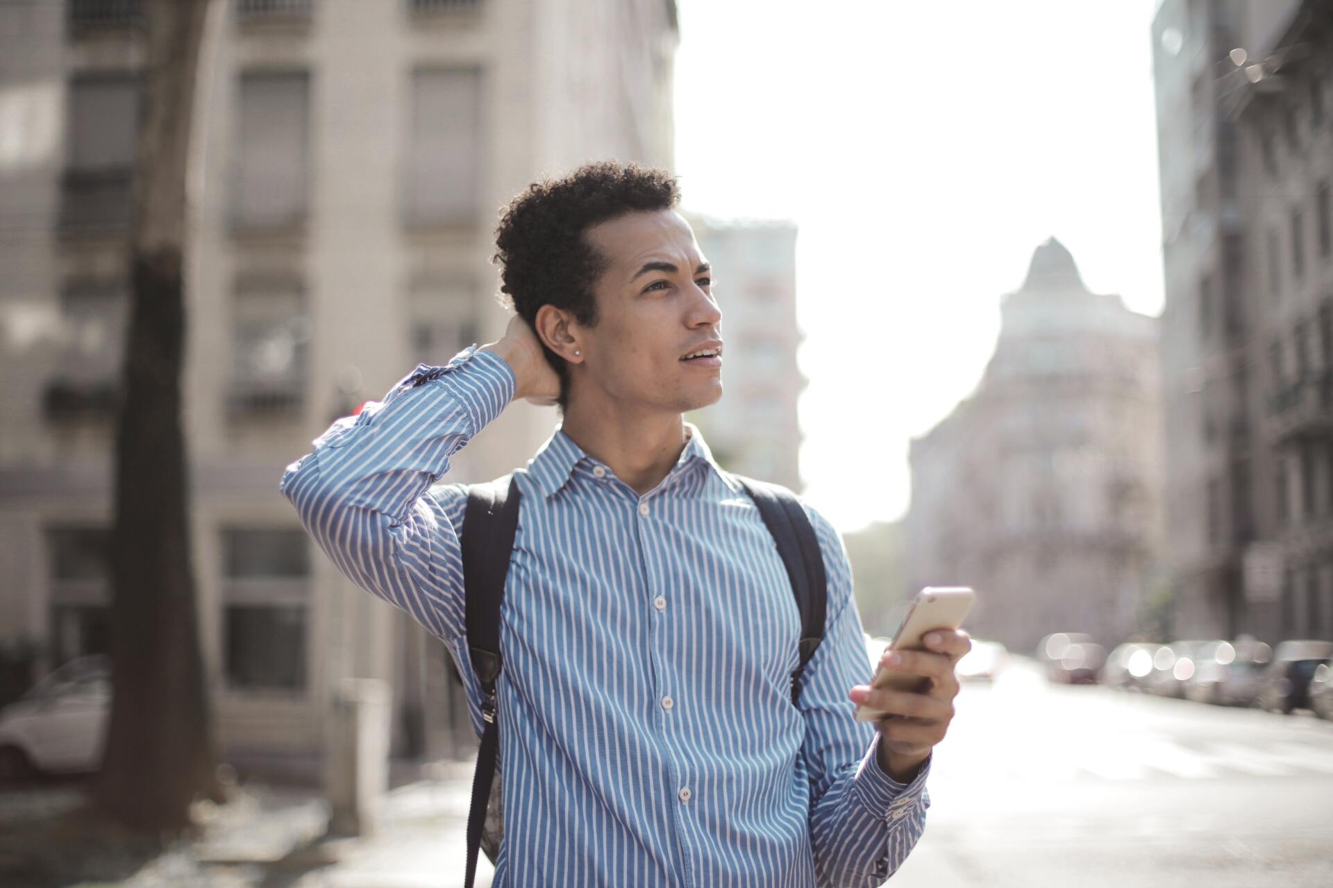 a man with a backpack is walking down the street while looking at his cell phone .