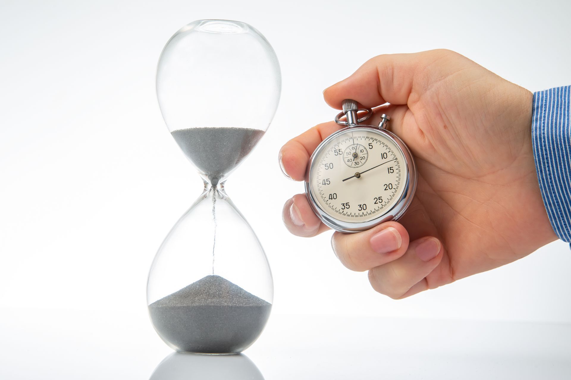 stopwatch with hourglass A person is holding a stopwatch in front of an hourglass.