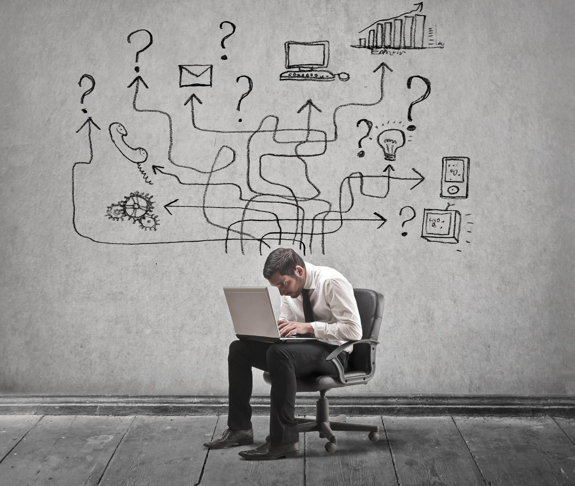 A man is sitting in a chair with a laptop in front of a wall with drawings on it