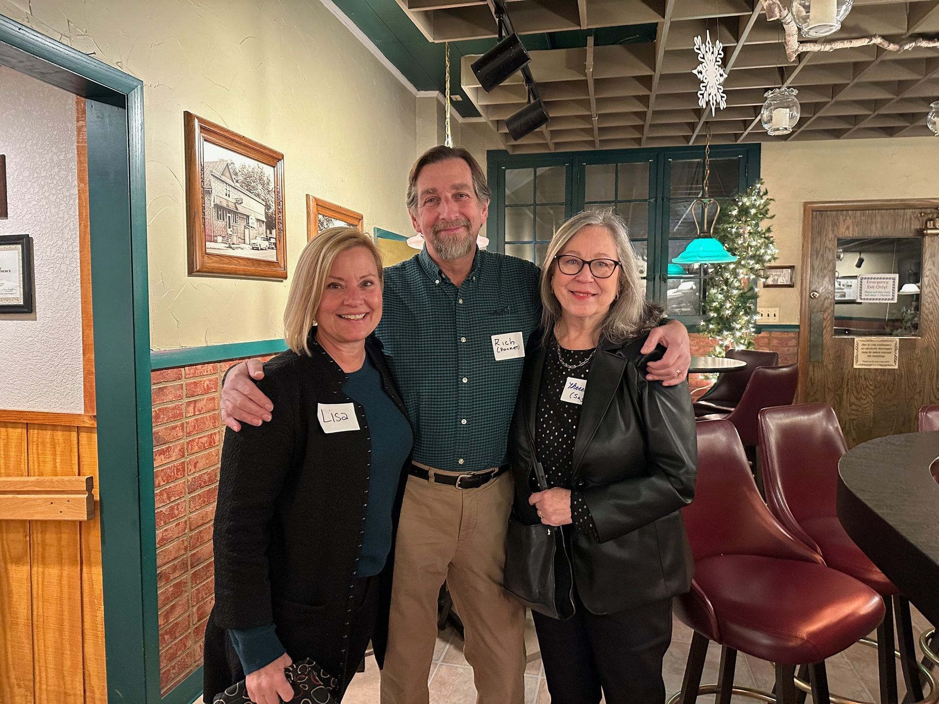 Three people pose for a photo inside a bar; two women flank a man, all smiling. The man has his arm around each woman's shoulder.