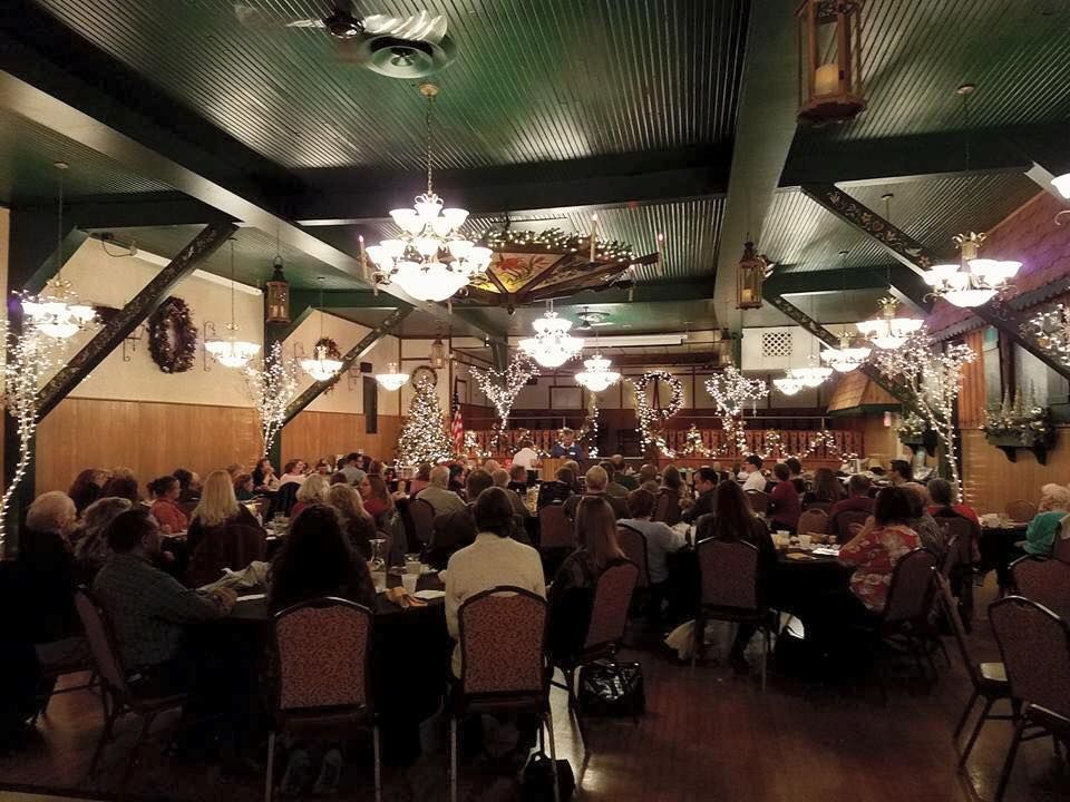A large room with many people seated at tables, decorated with chandeliers and string lights.