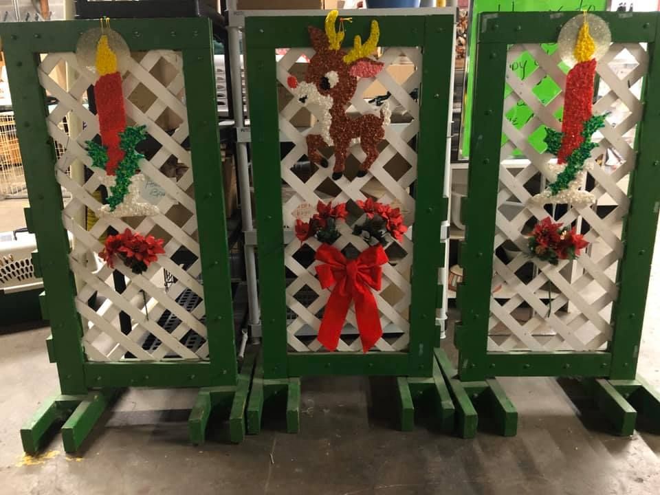 Three white lattice panels with green frames, decorated for Christmas with plastic candle lights, a reindeer, and a wreath with a red bow.