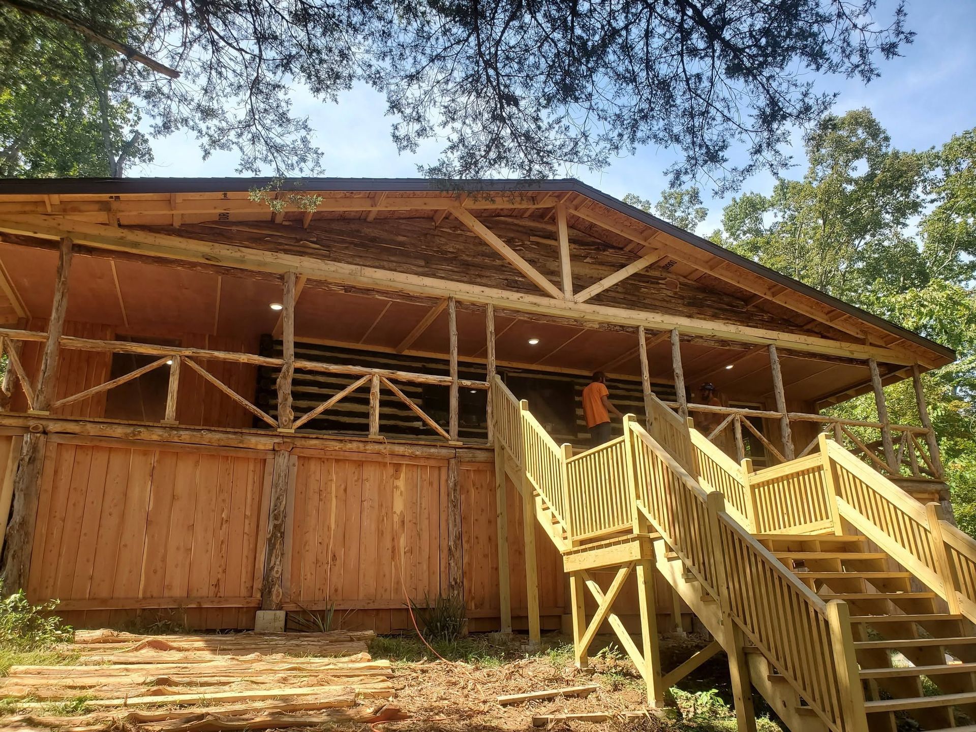 Wooden cabin with a large porch and stairs under trees in bright sunlight