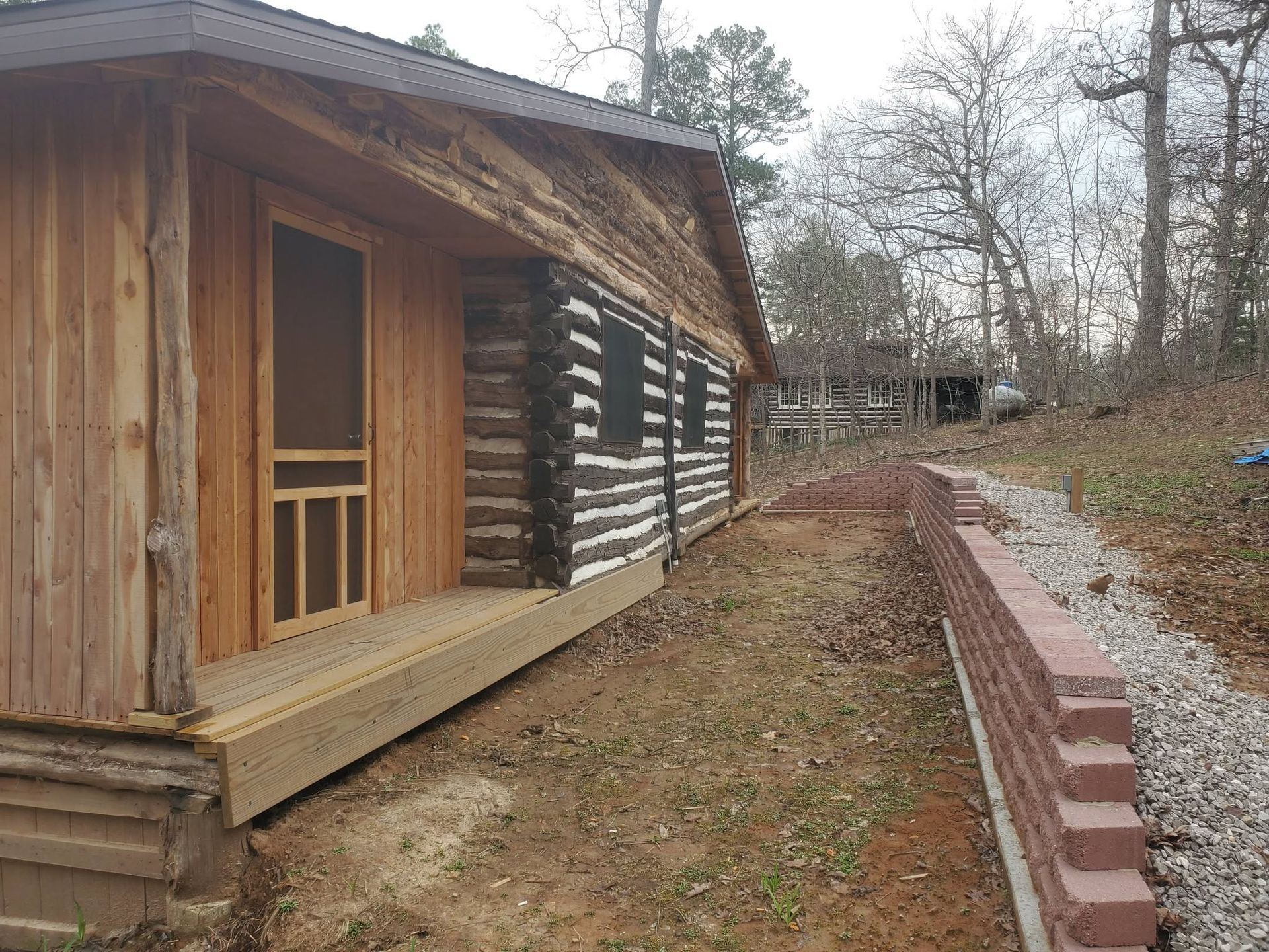Wooden cabin with porch beside a brick-lined path in a wooded yard
