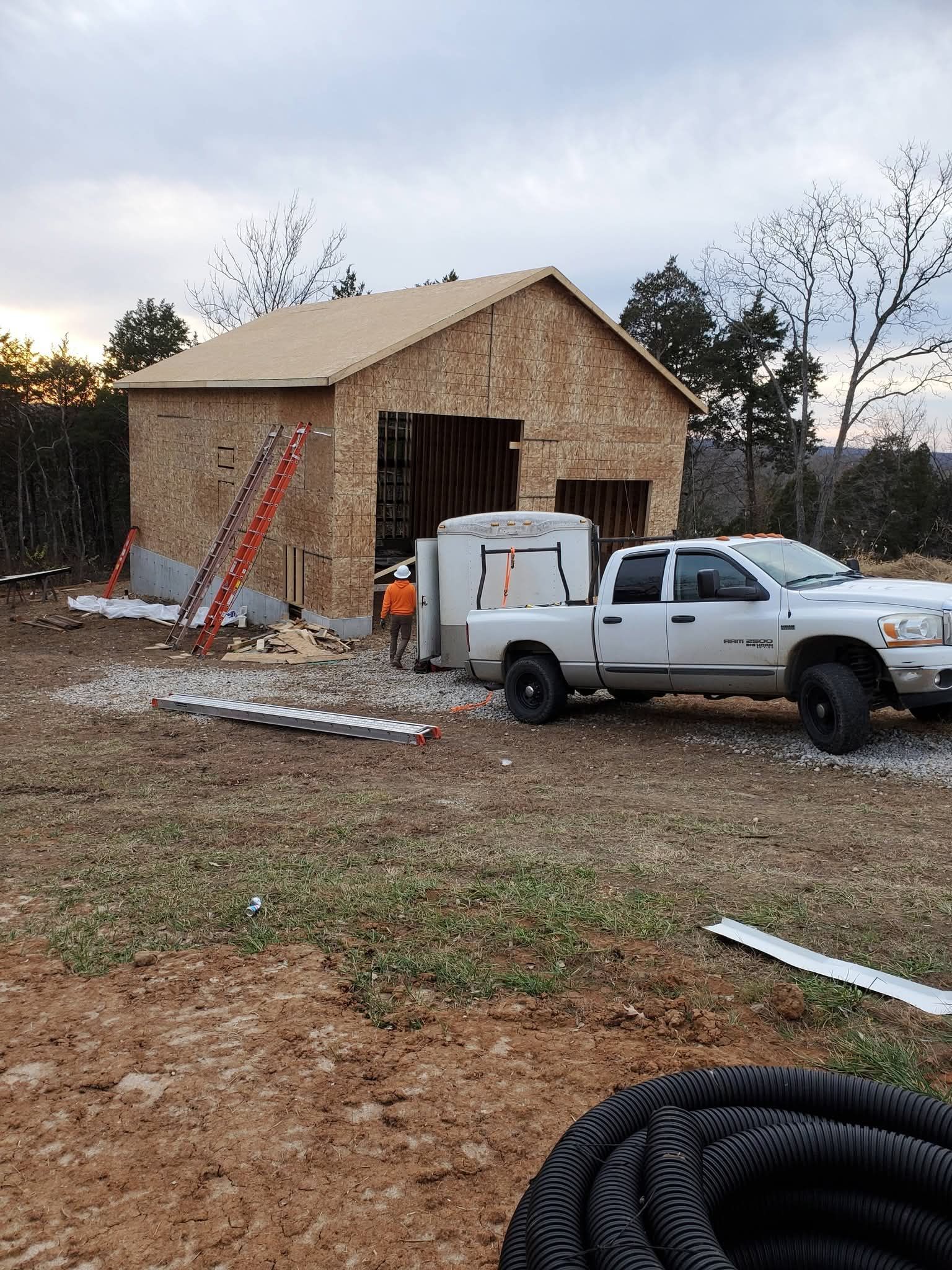 Pickup truck and trailer beside a partly built wooden shed at a muddy construction site.