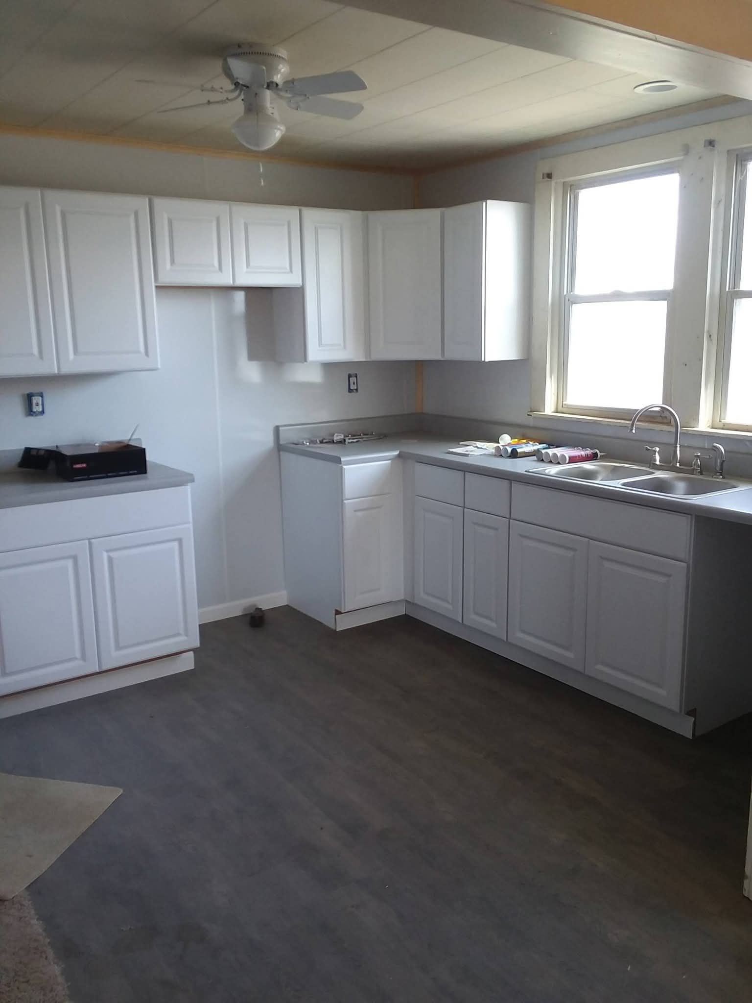 Empty white kitchen with cabinets, sink, stove, and two windows letting in daylight