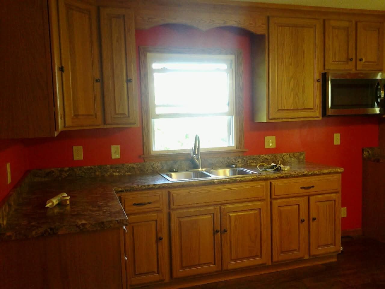 Wooden kitchen with red walls, granite counters, and a bright window over the sink