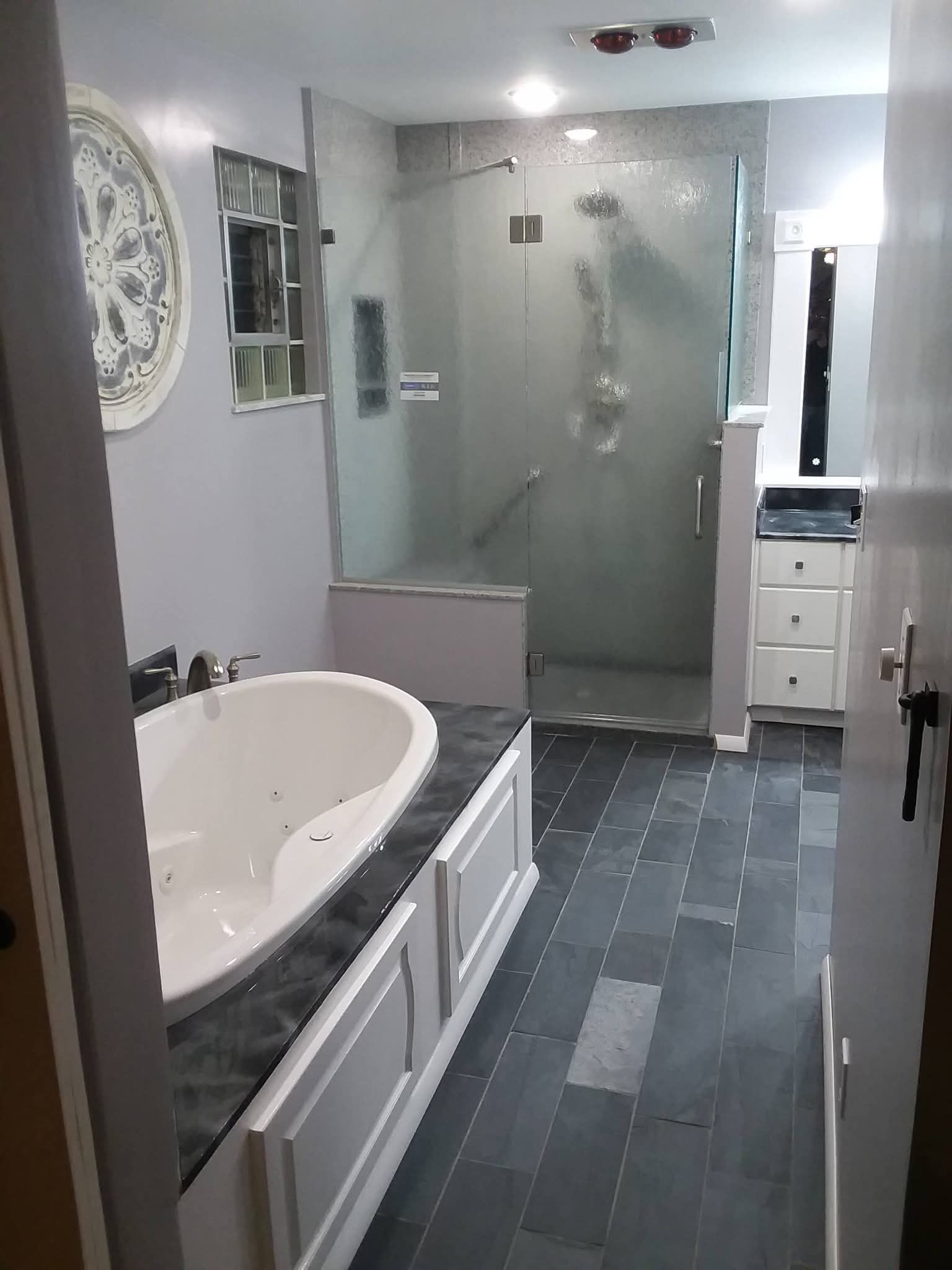 Modern bathroom with white vanity, oval tub, glass shower, and gray tile flooring.