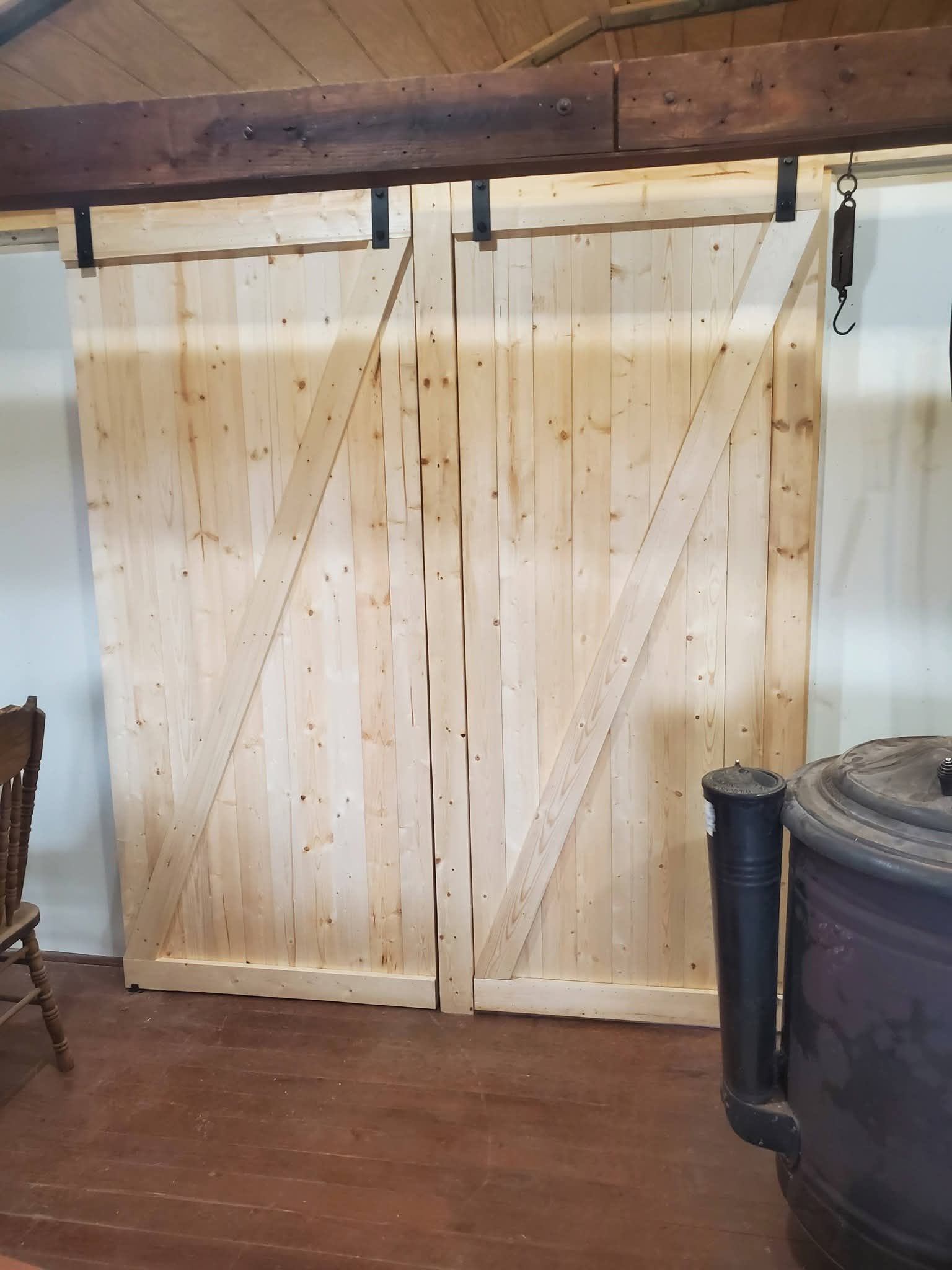 Wooden barn-style sliding doors in a rustic room with dark wood flooring and a stove on the right.