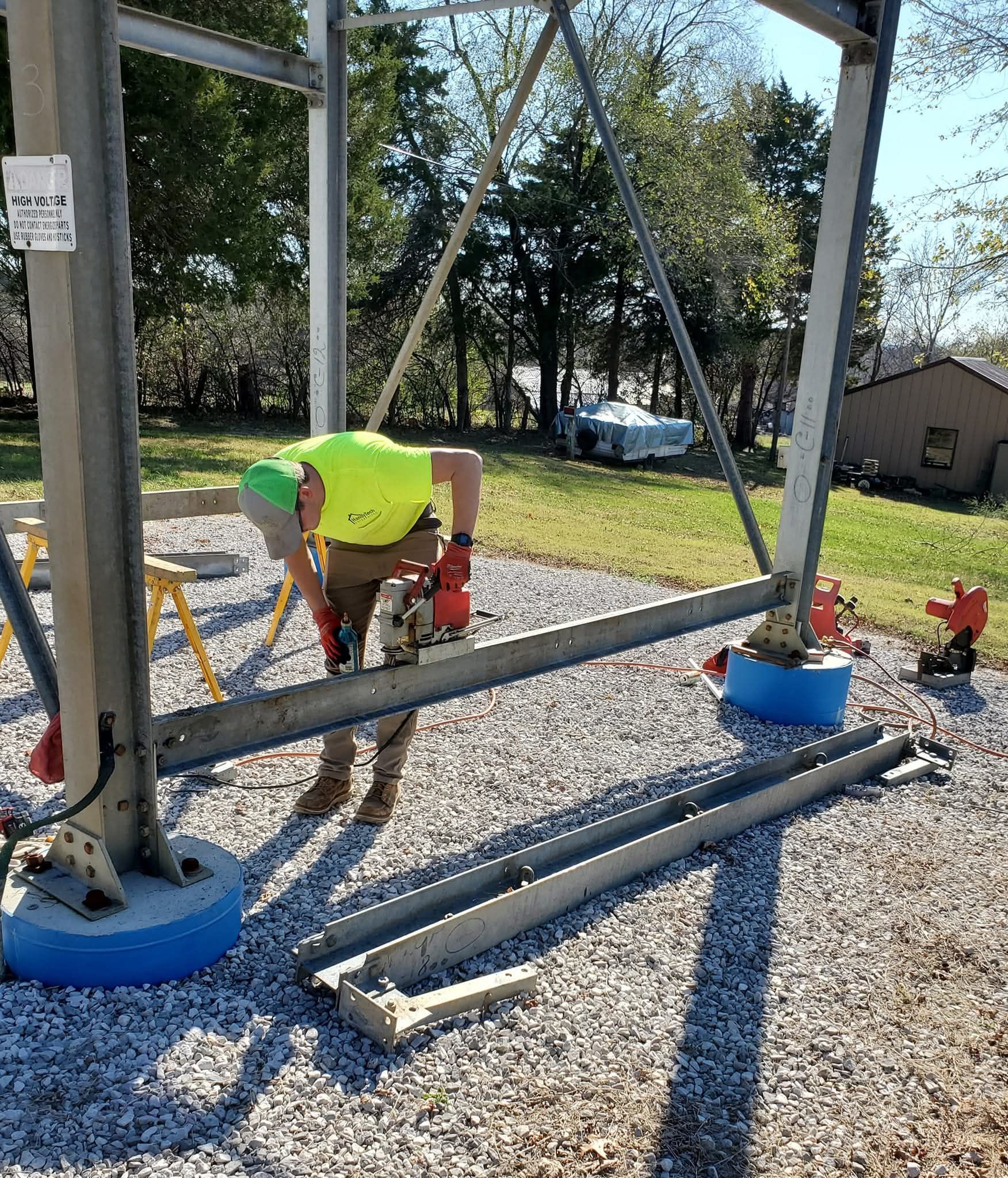 Worker in neon shirt using red power tool on metal frame at a construction site