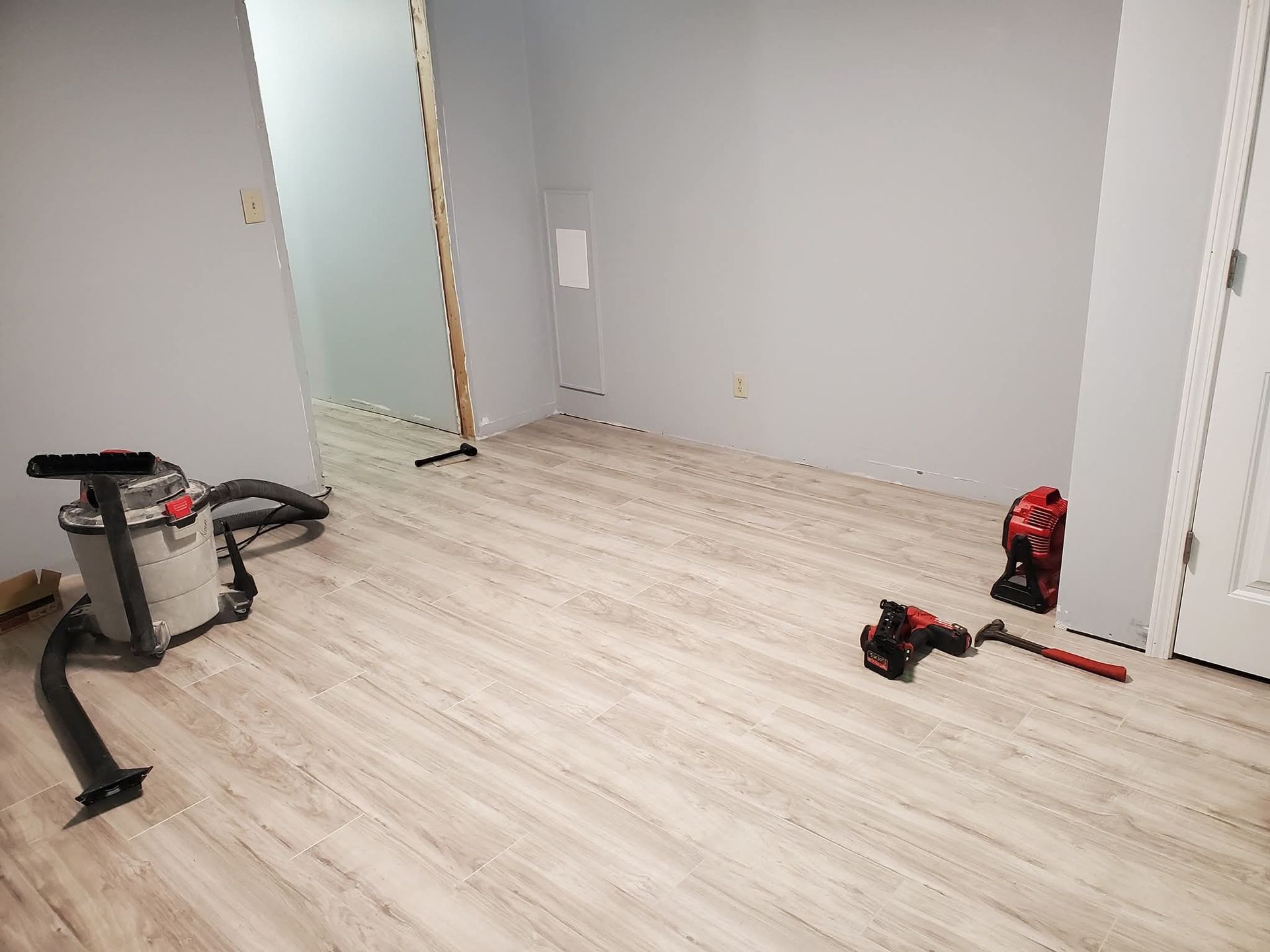 Empty room with light wood floors, gray walls, and cleaning tools on the floor.