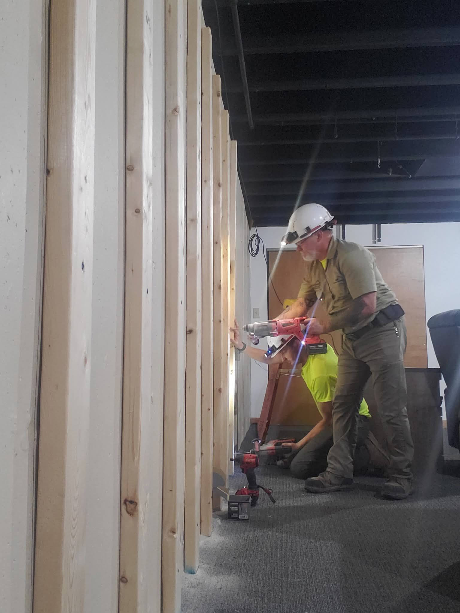 Worker in hard hat using a red floor machine inside a construction site room.