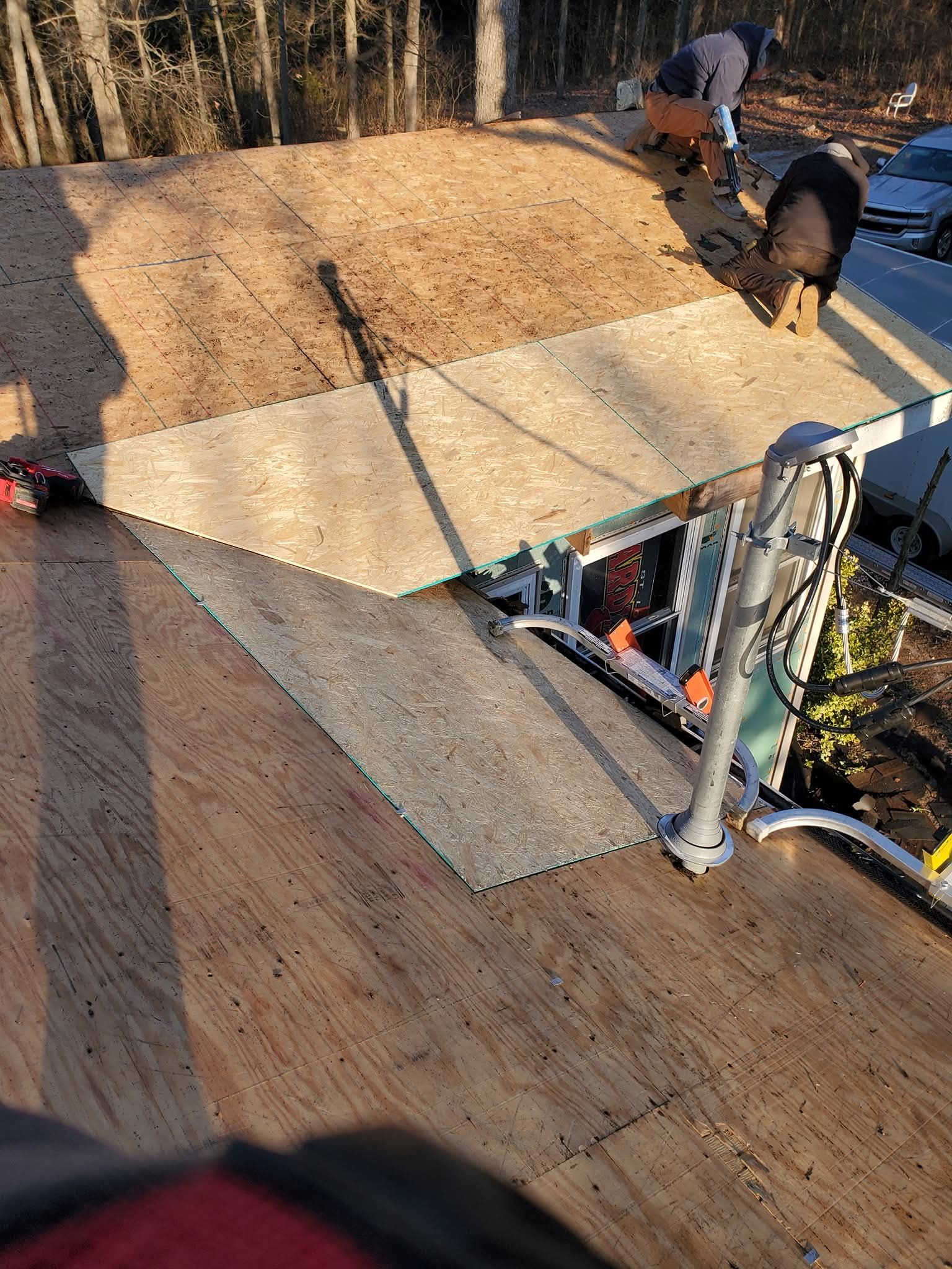 Workers installing plywood roofing on a house roof, with unfinished sections and railing nearby.