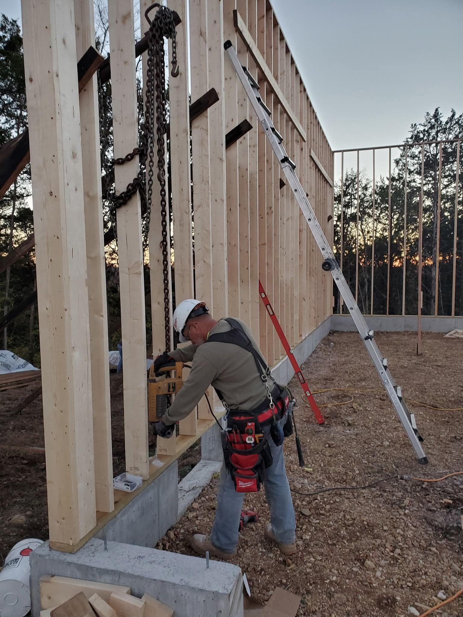 Worker fastening wooden wall framing at a construction site, with ladders and tools nearby.