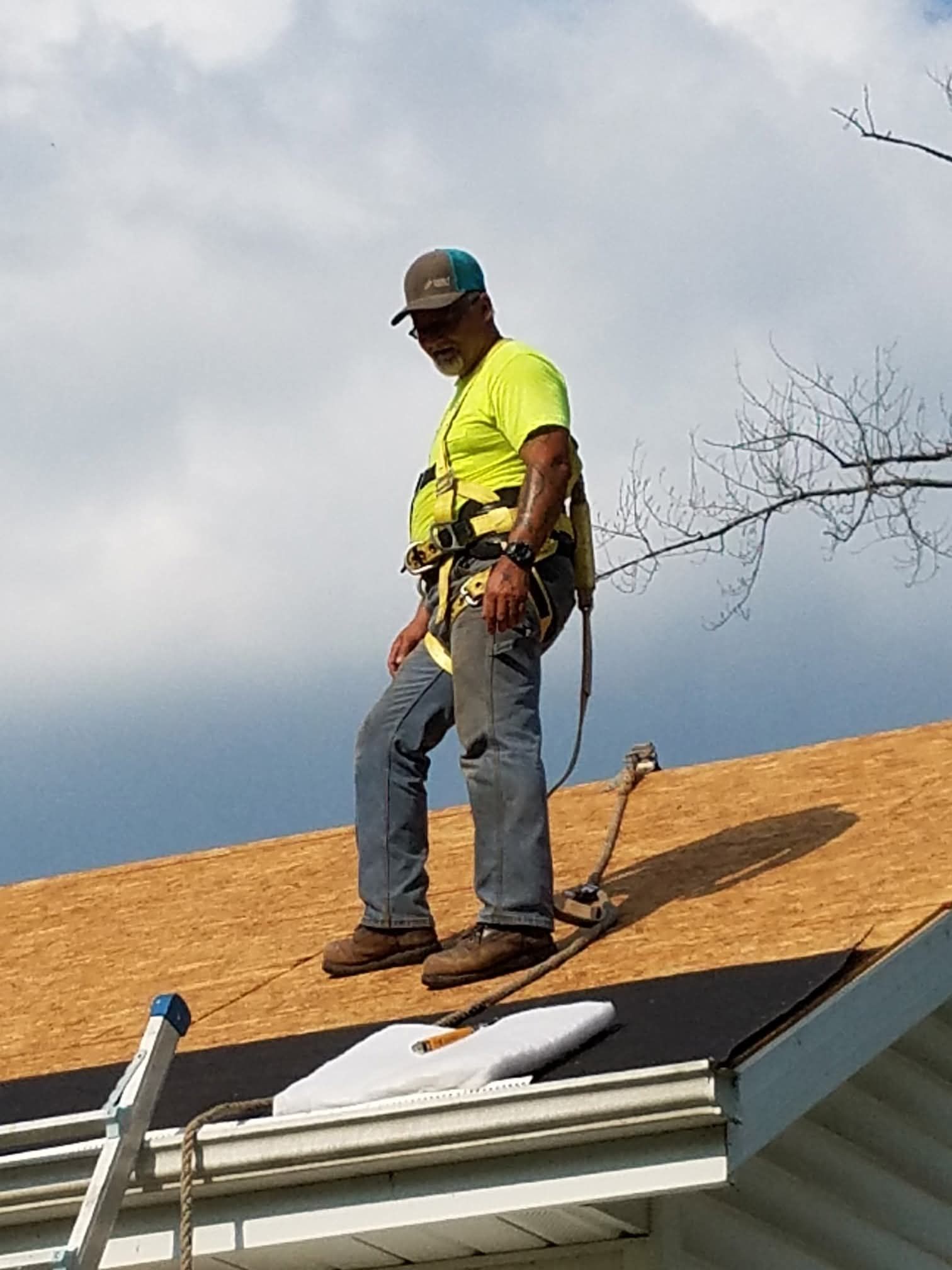 Worker in neon yellow shirt installing roofing on a house roof under a cloudy sky