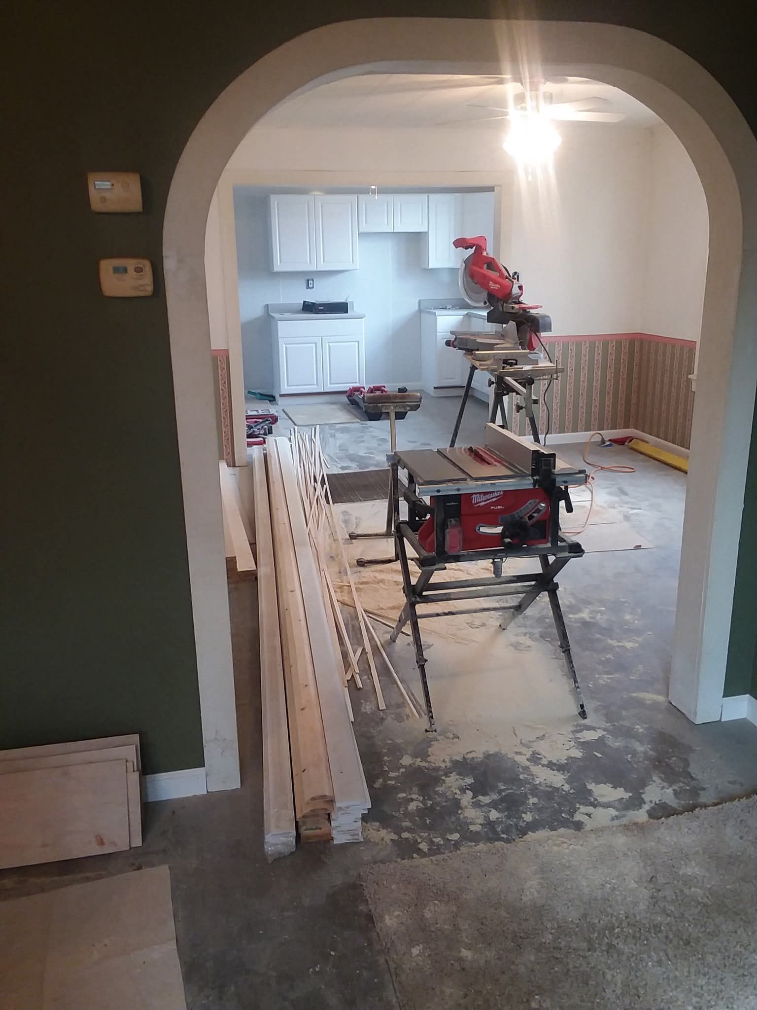 Renovation scene with saws and lumber in a hallway leading to a kitchen